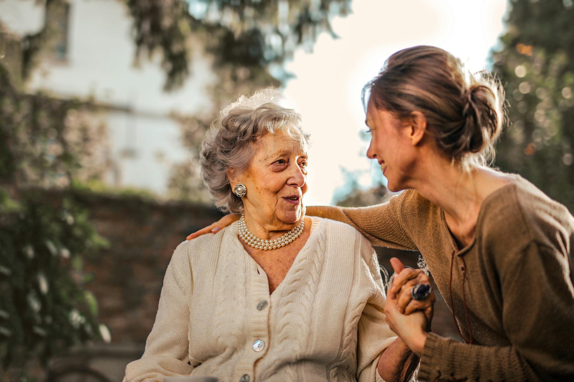 An older woman and a younger woman talking warmly together outdoors